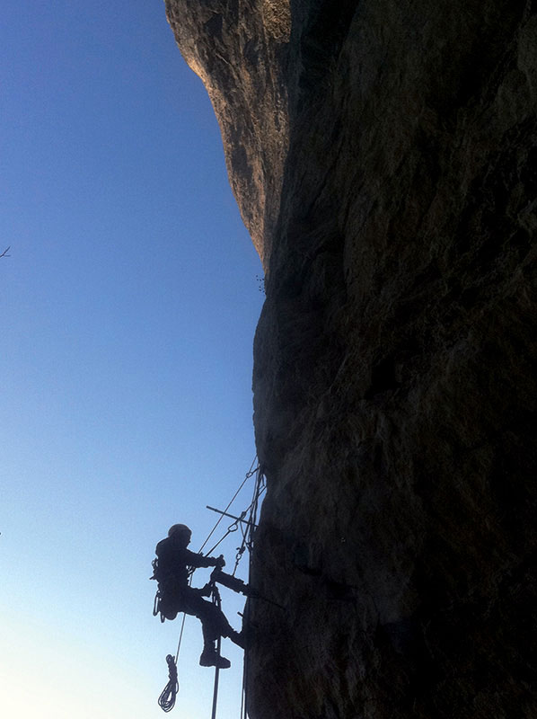 cordiste au travail sur une falaise en contre-jour